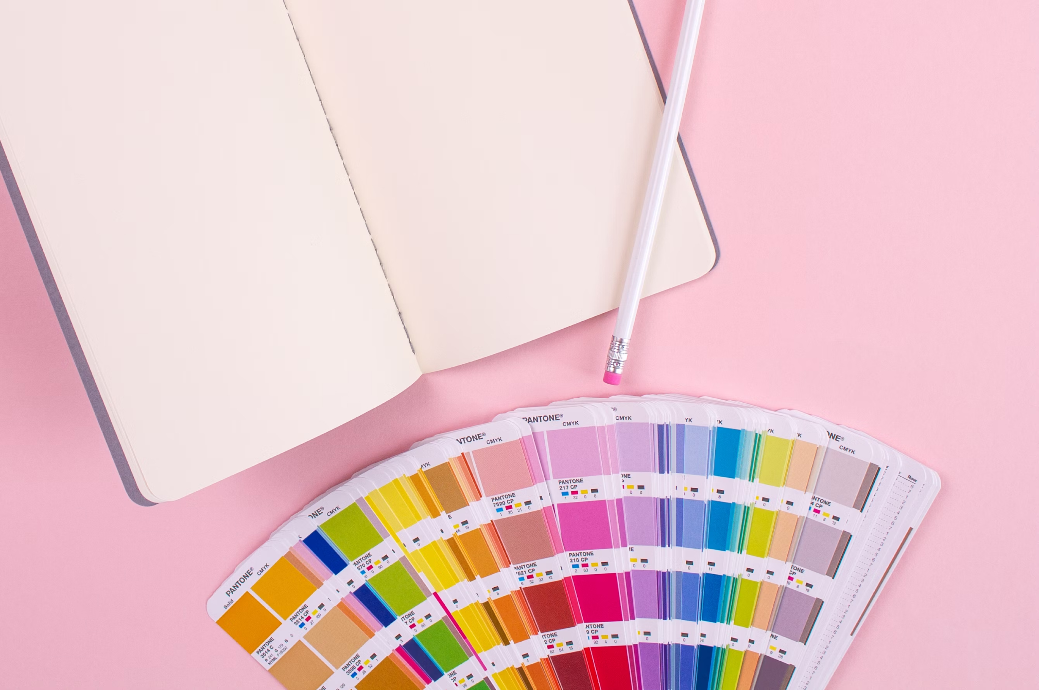 Photo of an open notebook, a pencil, and a color fan deck on a table.